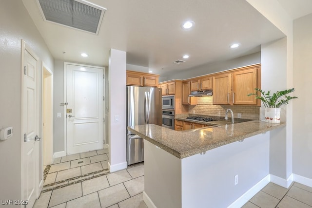 kitchen featuring dark stone countertops, appliances with stainless steel finishes, kitchen peninsula, light tile patterned floors, and tasteful backsplash