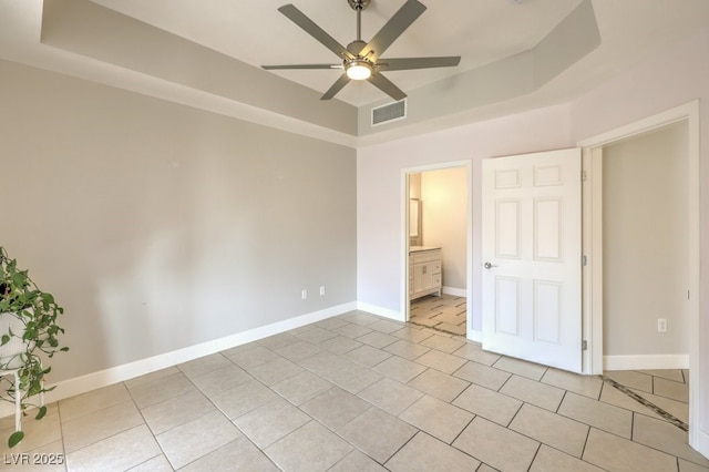 unfurnished bedroom featuring a raised ceiling, ceiling fan, light tile patterned flooring, and connected bathroom