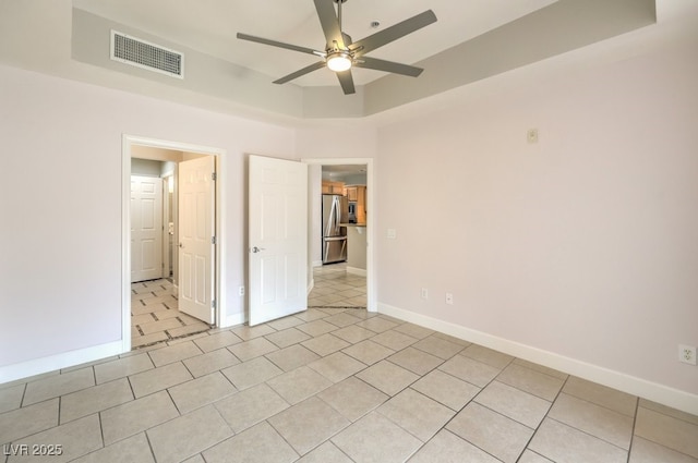 unfurnished bedroom with stainless steel refrigerator, ceiling fan, light tile patterned floors, and a tray ceiling