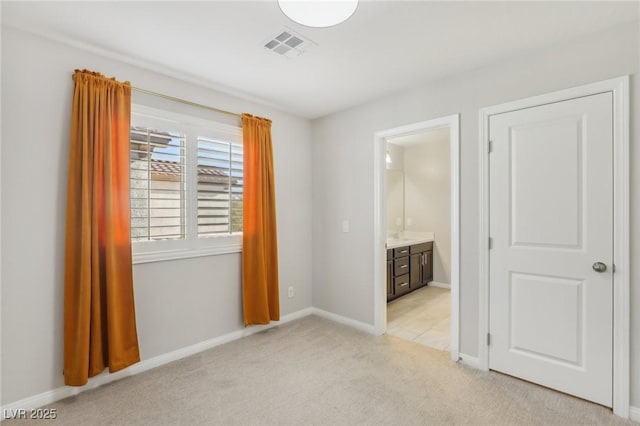 unfurnished bedroom featuring light colored carpet and ensuite bath