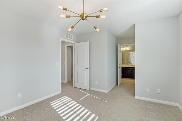 unfurnished bedroom with ensuite bathroom, light colored carpet, and an inviting chandelier