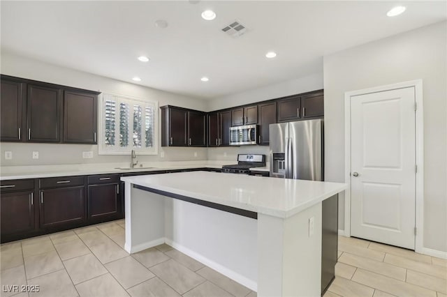 kitchen featuring appliances with stainless steel finishes, a kitchen island, sink, light tile patterned flooring, and dark brown cabinets