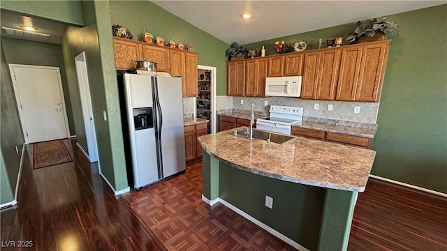 kitchen with white appliances, an island with sink, tasteful backsplash, lofted ceiling, and sink