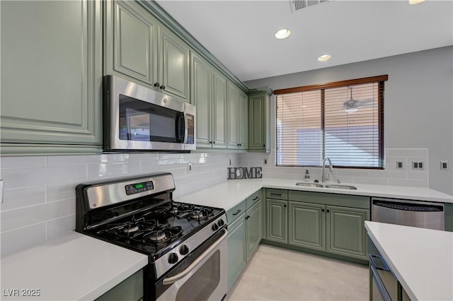 kitchen featuring appliances with stainless steel finishes, green cabinetry, backsplash, and sink