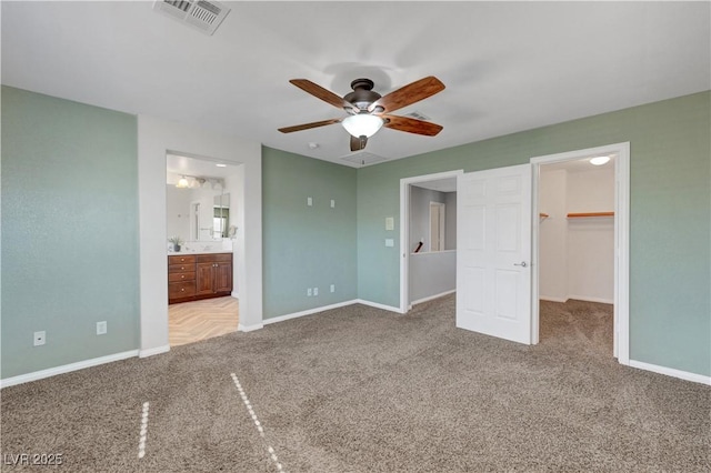 unfurnished bedroom featuring a closet, ensuite bath, light colored carpet, ceiling fan, and a spacious closet