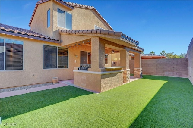 rear view of house with ceiling fan, a patio area, and a lawn