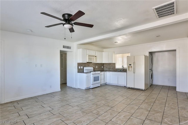 kitchen featuring white appliances, stacked washer / drying machine, white cabinets, and sink