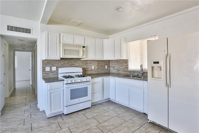 kitchen featuring white appliances, backsplash, white cabinets, dark stone counters, and sink