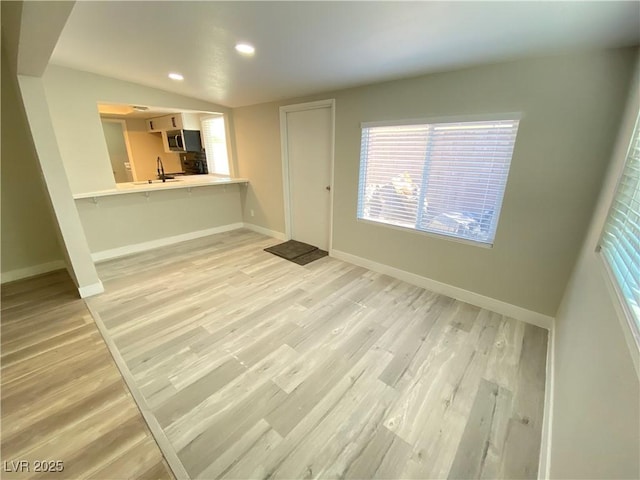 unfurnished living room featuring sink, light hardwood / wood-style flooring, and lofted ceiling