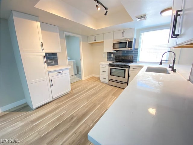 kitchen with a raised ceiling, washer / dryer, white cabinets, appliances with stainless steel finishes, and sink