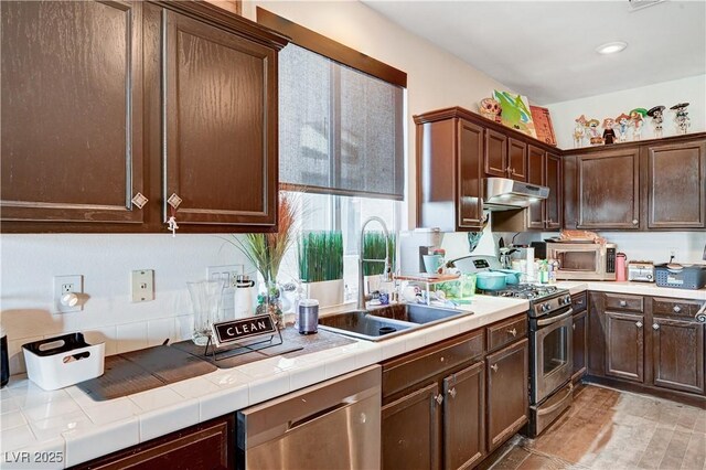 kitchen featuring appliances with stainless steel finishes, tile counters, sink, and dark brown cabinetry