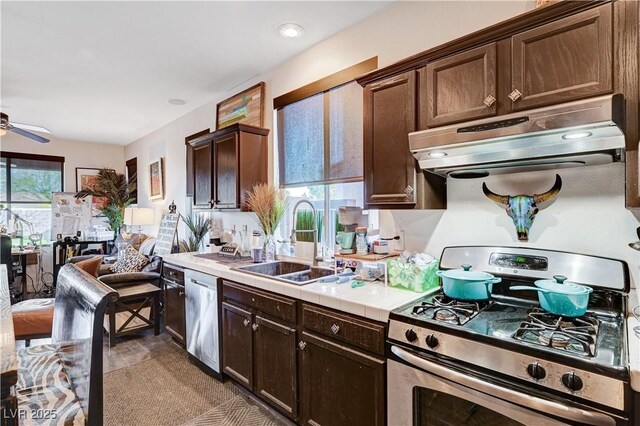 kitchen with stainless steel appliances, ceiling fan, tile countertops, sink, and dark brown cabinets