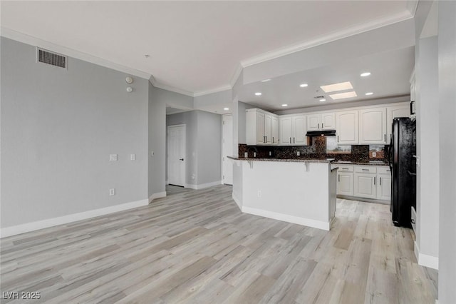 kitchen featuring light hardwood / wood-style floors, ornamental molding, black fridge, white cabinetry, and tasteful backsplash