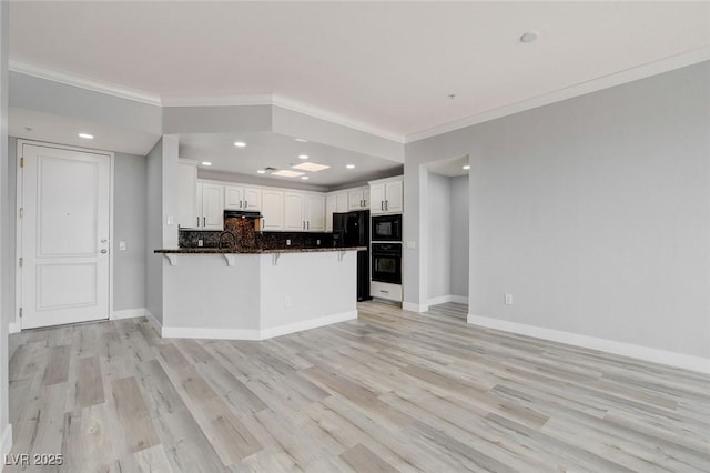 kitchen featuring white cabinetry, kitchen peninsula, backsplash, dark stone counters, and black appliances