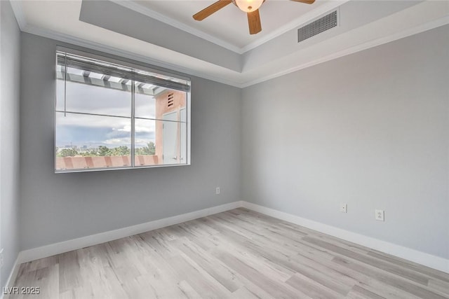 empty room with ornamental molding, light wood-type flooring, ceiling fan, and a tray ceiling