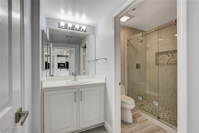 bathroom featuring a textured ceiling, hardwood / wood-style floors, toilet, a shower with door, and vanity