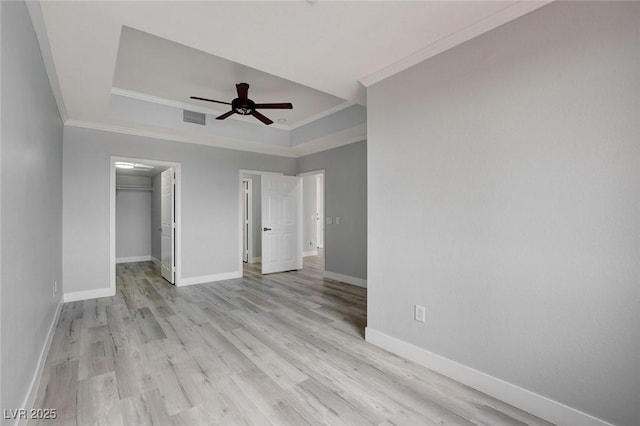 unfurnished bedroom featuring ceiling fan, a spacious closet, crown molding, and a tray ceiling