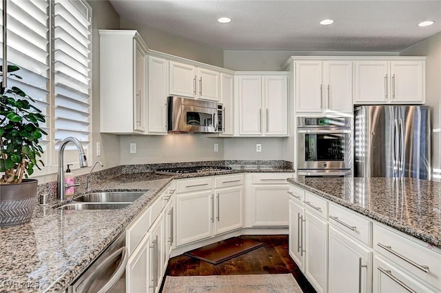 kitchen with light stone counters, stainless steel appliances, white cabinetry, and sink