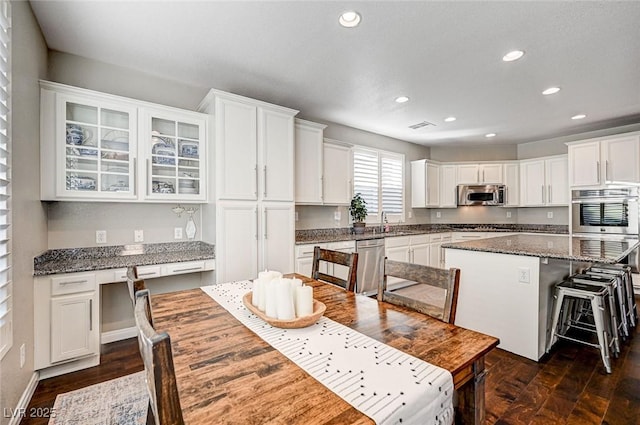 kitchen featuring stainless steel appliances, white cabinets, a center island, dark stone counters, and a breakfast bar