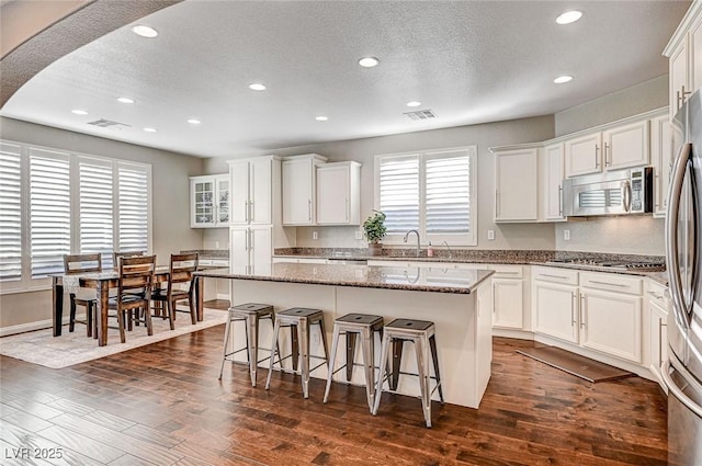 kitchen with a center island, a kitchen bar, white cabinetry, dark stone counters, and appliances with stainless steel finishes