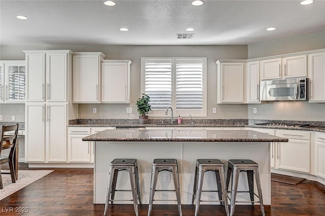 kitchen with appliances with stainless steel finishes, a center island, dark stone counters, dark hardwood / wood-style floors, and white cabinets