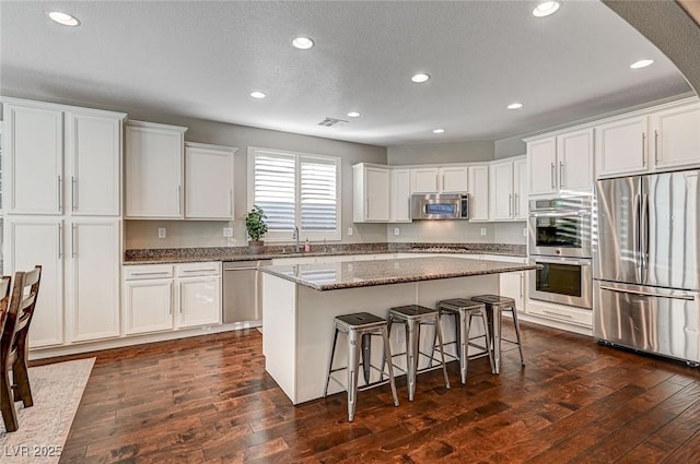 kitchen with dark stone countertops, stainless steel appliances, a center island, dark hardwood / wood-style flooring, and white cabinetry