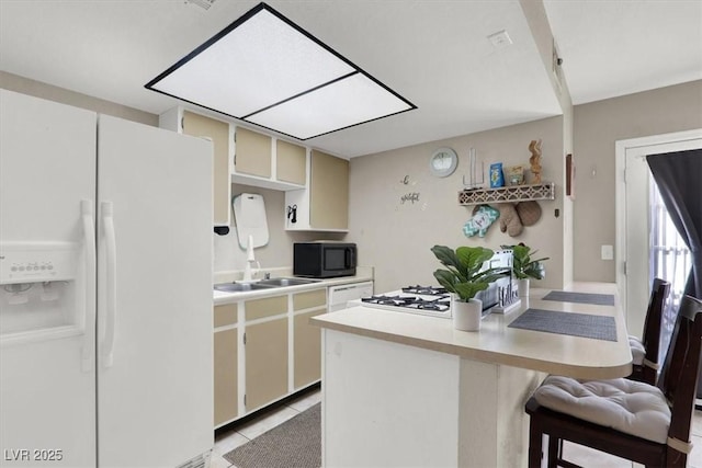 kitchen with white fridge with ice dispenser, light tile patterned flooring, cream cabinetry, and a kitchen breakfast bar