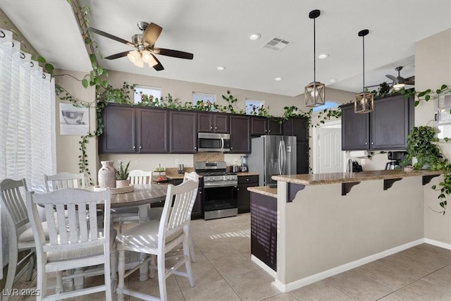 kitchen featuring decorative light fixtures, appliances with stainless steel finishes, light tile patterned flooring, and light stone counters