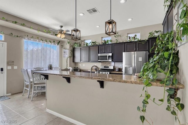 kitchen with light stone countertops, a kitchen breakfast bar, hanging light fixtures, stainless steel appliances, and dark brown cabinets