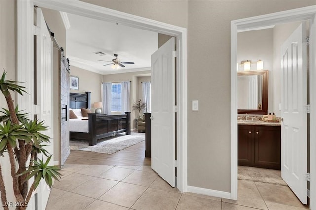 tiled bedroom with ornamental molding, ceiling fan, connected bathroom, and a barn door