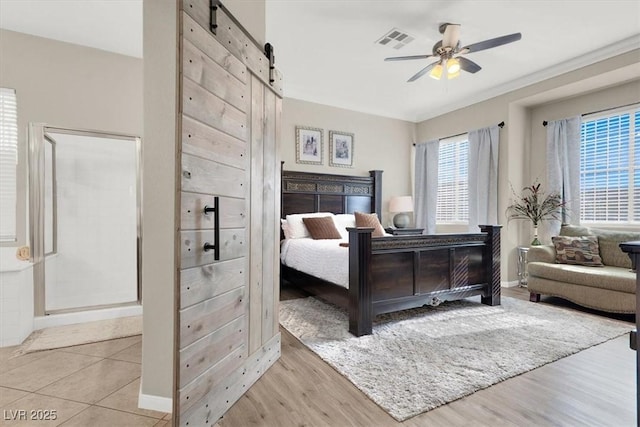 bedroom featuring ceiling fan, light hardwood / wood-style floors, and a barn door