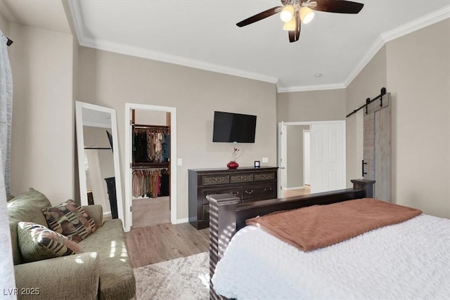 bedroom with connected bathroom, ceiling fan, light hardwood / wood-style flooring, a barn door, and crown molding