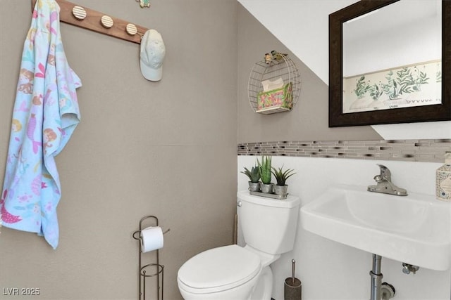 bathroom featuring toilet, decorative backsplash, and sink