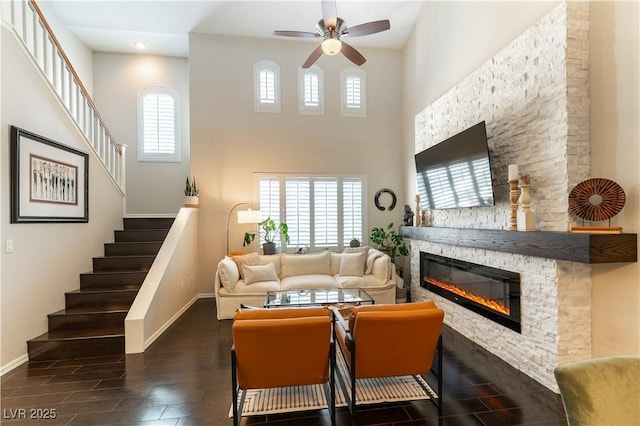 living room featuring ceiling fan, a fireplace, and a high ceiling