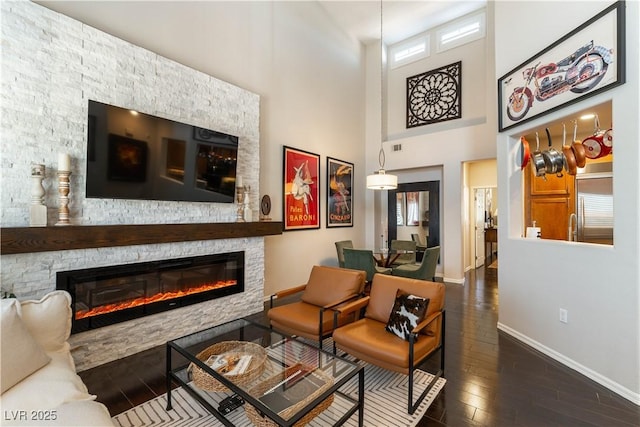 living area featuring a towering ceiling, dark hardwood / wood-style floors, and a stone fireplace