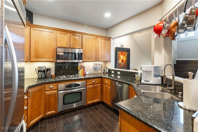 kitchen with stainless steel appliances, sink, kitchen peninsula, decorative backsplash, and dark stone counters