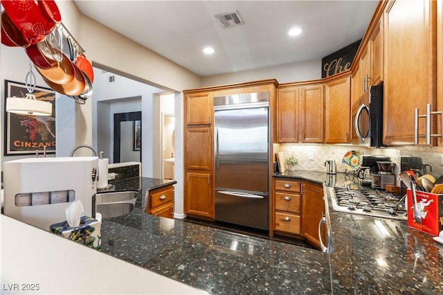 kitchen with stainless steel appliances, decorative backsplash, dark stone countertops, and kitchen peninsula