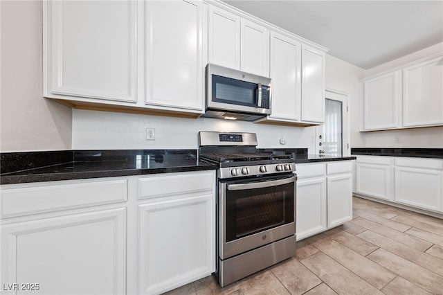 kitchen with appliances with stainless steel finishes, white cabinetry, dark stone countertops, and light wood-type flooring