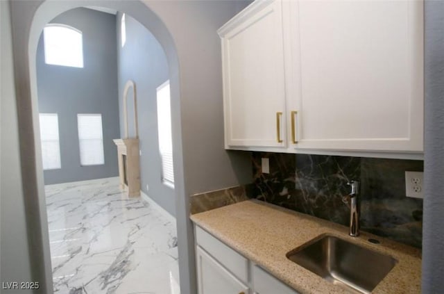 bar with light stone counters, white cabinets, tasteful backsplash, and sink