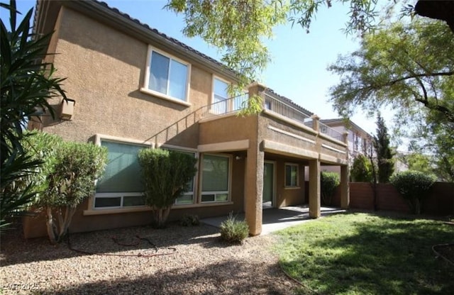 rear view of house with a balcony, a yard, and a patio area