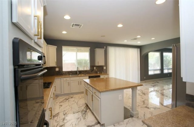 kitchen with sink, white cabinetry, backsplash, and a kitchen island