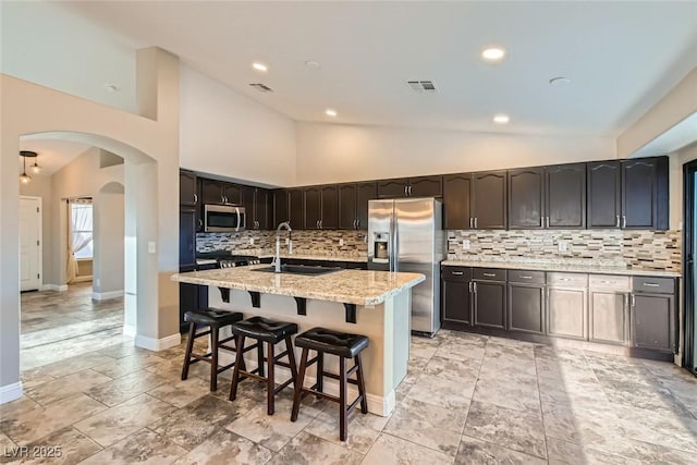 kitchen featuring light stone countertops, stainless steel appliances, high vaulted ceiling, a kitchen island with sink, and sink