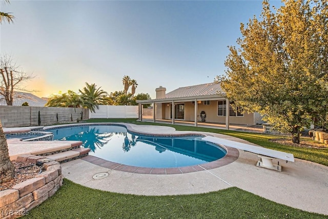 pool at dusk with a diving board, a patio area, and an in ground hot tub