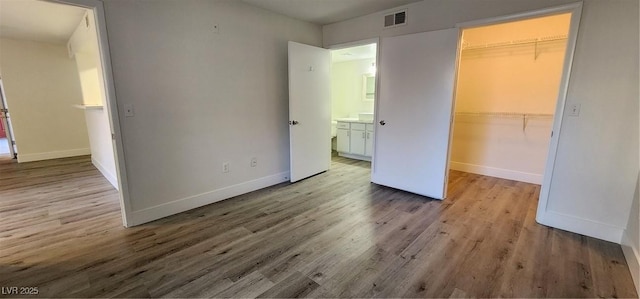 unfurnished bedroom with a spacious closet, a closet, and wood-type flooring