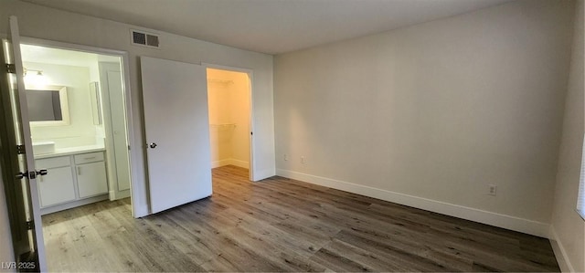 unfurnished bedroom with ensuite bathroom, light hardwood / wood-style floors, a spacious closet, and a closet