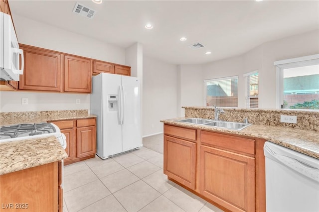 kitchen with light tile patterned floors, sink, light stone counters, and white appliances