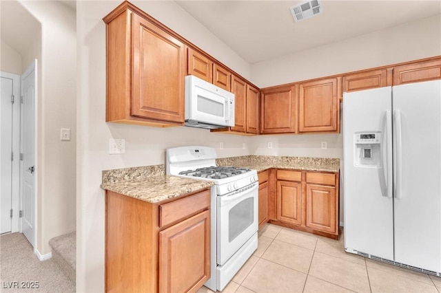 kitchen featuring light tile patterned floors, light stone counters, and white appliances