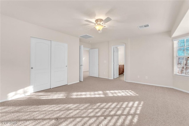 unfurnished bedroom featuring ceiling fan, light colored carpet, a closet, and ensuite bathroom