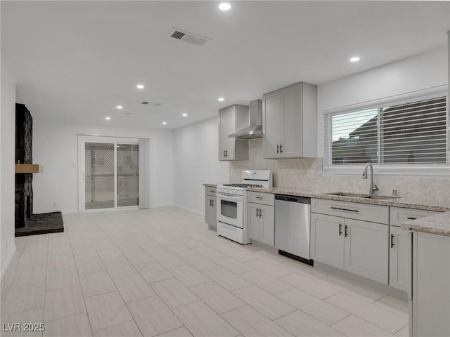 kitchen featuring decorative backsplash, sink, wall chimney range hood, stainless steel dishwasher, and white gas stove