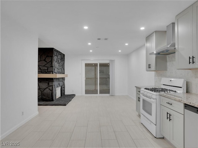 kitchen featuring light stone counters, white gas range, stainless steel dishwasher, wall chimney exhaust hood, and decorative backsplash